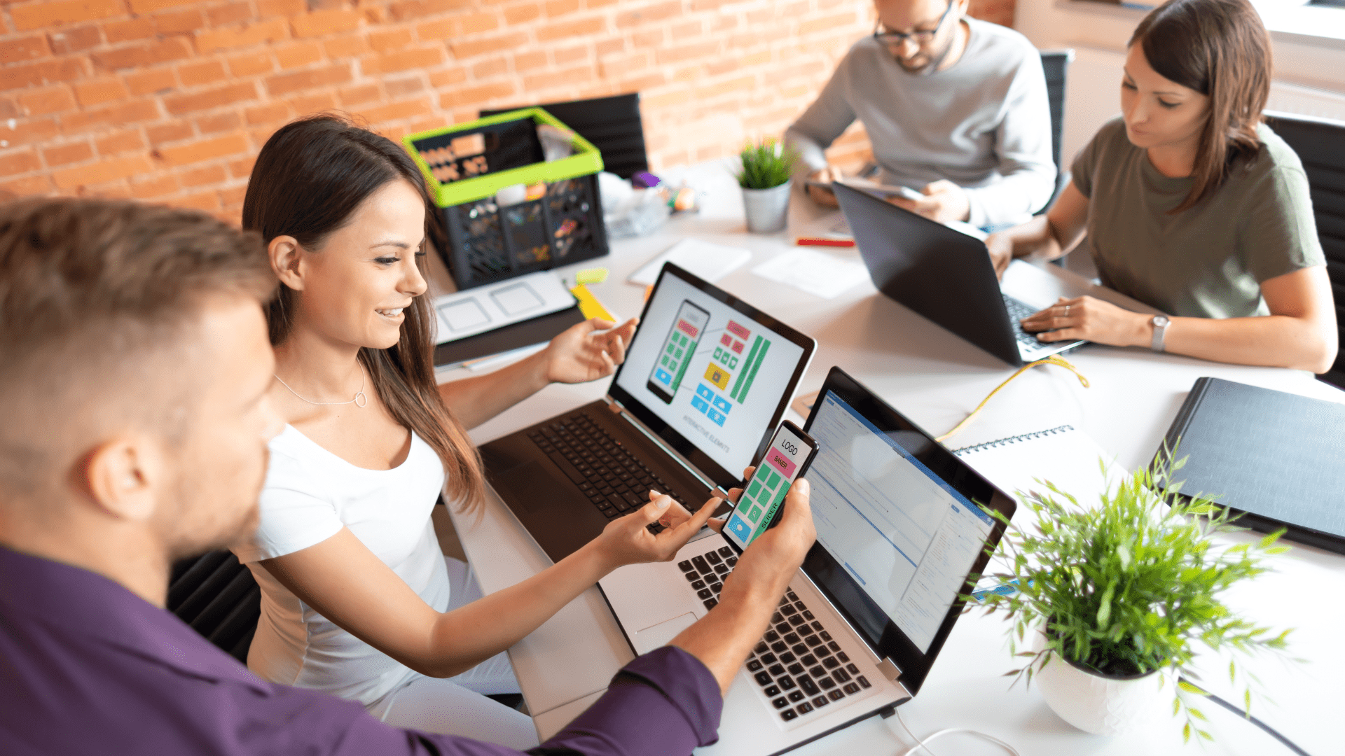 Turbo charge innovation using AI tools. Two females and two males are sat together at a desk using laptops and smart phones to review shared screens. 