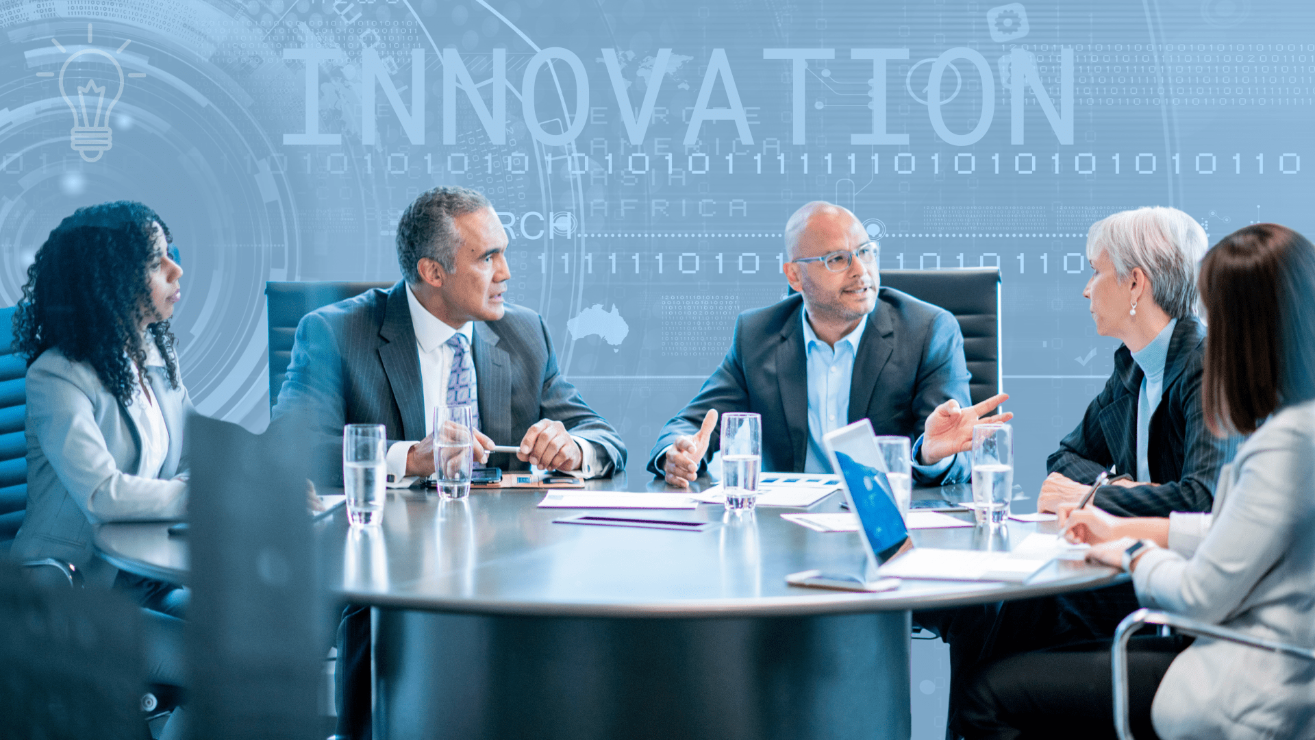 Turbocharge innovation using AI tools. Two men and three women dressed in smart business attire are sitting at a modern office table and are discussing a topic in ernest.